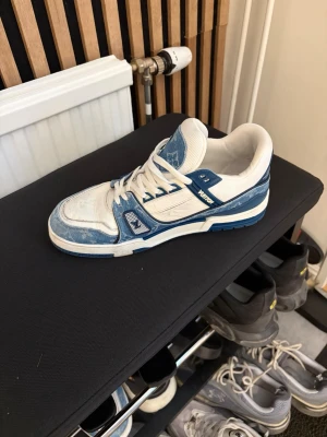 Blå vita sneakers med detalj  - Säljer ett par  sneakers i blått och vitt med denimdetaljer och tydligt -logga på plösen. Skorna har vita snören, blå sula och klassiska monogramdetaljer. Snygg retrovibe och riktigt statement-piece för dig som gillar exklusiva sneakers.
