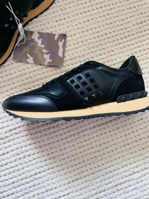 Svarta Valentino Rockrunners - Snygga svarta sneakers från Valentino, modellen är Rockrunners och dem är 9,5/10 skick, allt som ingår: dustbag, valentino kuvert, valentino kort, extra skosnören. Har ni frågor så är det bara o ställa dem direkt! Äktenhet garanteras ej men dem är checkade o ser äkta ut, en spik har gått av men annars är dem i ny skick o de e inget man märker att den har gått av