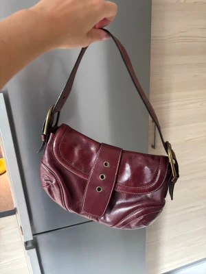 Vinröd axelremsväska i skinn - Köp secondhand 200kr, saknar spänne på framsidan tyvärr 