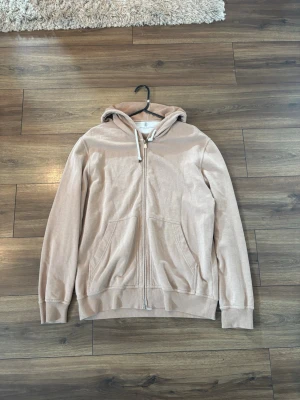 Beige hoodie från Brunello Cucinelli - Snygg beige hoodie från Brunello Cucinelli med dragkedja framtill, två stora fickor och justerbar huva med vita snören. Tillverkad i mjukt bomullsmaterial som känns riktigt skönt mot huden. Perfekt för en avslappnad och stilren look.