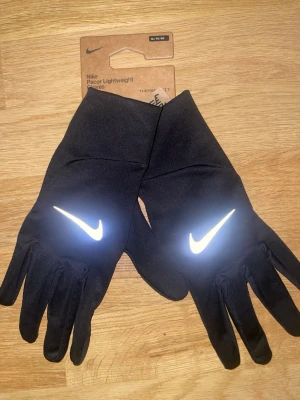 Svarta Nike Pacer handskar  - Svarta, lätta löparhandskar 🧤från Nike med reflekterande Swoosh-logga på ovansidan. Tillverkade i ett stretchigt syntetmaterial som andas och har touch-funktion på fingertopparna. Perfekta för löpning under kyliga dagar.                                                               Size:XL