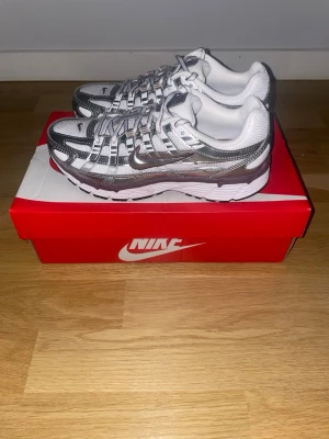 Nike P-6000 sneakers - Nike sneakers i silver och vitt med mesh- och syntetpaneler, klassisk swoosh på sidan och vita snören. Skorna har en chunky sula och sportig design som passar perfekt till streetwear och casual outfits.