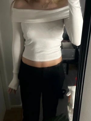 Vit offshoulder croppad topp - Trendig vit offshoulder topp med långa ärmar och croppad passform. Tunn och stretchig, perfekt att styla med höga byxor eller kjol. Enkel och stilren design som ger en snygg siluett.