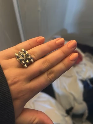 Silvrig ring med nitar - Cool ring i silverfärgad metall med flera små nitar i ett rutmönster. Ringen har en bred design och ger en edgy känsla till din stil. Perfekt för dig som gillar statement-smycken och vill sticka ut.
