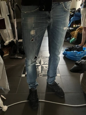 Ljusblå slitna jeans med hål ifrån Dondup, model GEORGE W33 - Säljer ett par ljusblå jeans med flera slitningar och hål på benen ifrån Dondup. Jeansen har en smal passform och klassisk femficksdesign. Perfekta för dig som gillar en avslappnad och trendig streetstil. A=41cm B=103cm, W33