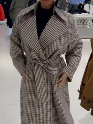 Zara oversized trenchcoat - Snygg trenchcoat i beige och brunt rutigt mönster. Jackan har bred krage, knytbälte i midjan och klassisk lång passform. Tillverkad i ett vävt material som ger en stilren look. Perfekt för dig som vill ha en trendig och tidlös ytterjacka.