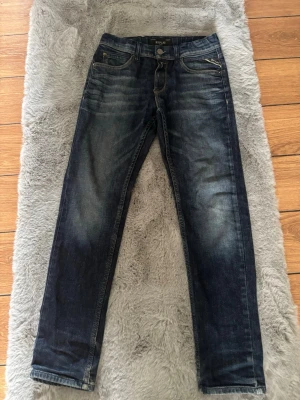 Mörkblå Replay jeans med raka ben - Snygga mörkblå jeans från Replay med raka ben och klassisk femficksmodell. Jeansen har slitningar och ljusare partier framtill för en cool, använd look. Tillverkade i denim med kontrastsömmar och dragkedja. Perfekta för en avslappnad stil.