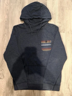 Hollister California Tunn Hoodie Blå Strl M (Passar L) - Hollister California blå tunn hoodie med randig bröstficka och knappdetalj, märkt storlek M men passar bättre som en normal L. Axelbredd 45,5 cm, bröstvidd 58,5 cm, armlängd 68 cm, midja 48 cm, längd 71,5 cm, i fint skick.
