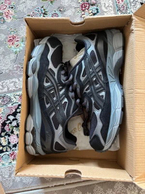 Asics gel nyc  - Snygga sneakers från Asics i svart och grått med mesh- och mockadetaljer. Skorna har en chunky sula och klassisk snörning. Perfekta för dig som gillar sportig stil och vill ha bekväma skor till vardags.