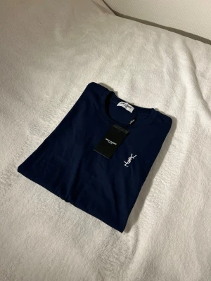 Mörkblå YSL t-shirt med logga - Snygg mörkblå t-shirt från Saint Laurent med klassisk vit YSL-logga broderad på bröstet. T-shirten har rund hals och korta ärmar, perfekt för en clean och stilren look. Tillverkad i mjuk bomull för maximal komfort.