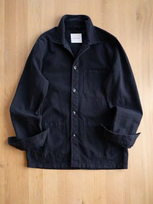 Black Chore Jacket, size S - Snygg svart overshirt från Lazy Arms i kraftigt bomullstyg. Klassisk krage, tre utanpåliggande fickor och knäppning med fyra knappar framtill. Långärmad modell med avslappnad passform, perfekt för lager på lager och en clean look.