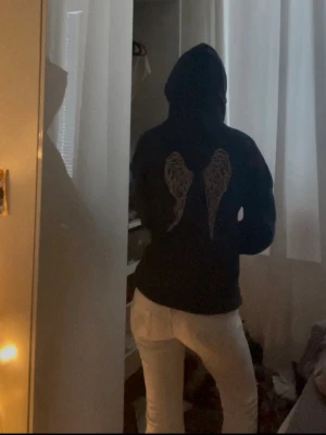 Marinblå hoodie med änglavingar - Säljer en marinblå hoodie med huva och tryckta änglavingar på ryggen. På bröstet står det 'the Queen' i vit text. Hoodien har en avslappnad passform och är perfekt för en chill och stilren look.