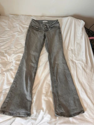 Grå bootcut jeans - Säljer ett par gråa bootcut jeans och klassiska fem fickor. Jeansen har en snygg tvätt och utsvängda ben, perfekta för en trendig och avslappnad stil. Materialet är denim med synliga sömmar.