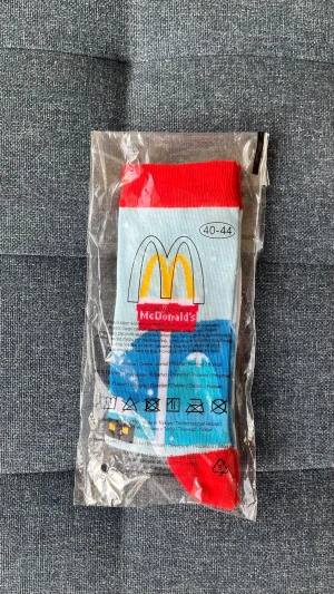 Färgglada McDonald's strumpor 40-44 - Säljer ett par färgglada strumpor med McDonald's-logga i storlek 40-44. Strumporna har röd mudd och tå, ljusblå och vita partier samt gula detaljer. Tillverkade i mjuk bomullsmix och perfekta för dig som vill sticka ut med coola detaljer.