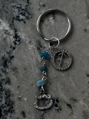 Handgjord nyckelring Skytten/Sagittarius ♐️ - Handgjord nyckelring med stjärntecknet Skytten. Turquoise färgade blå apatit kristallchips för att symbolisera Skyttens birthstone Turquoise. Och en Hello Kitty charm!