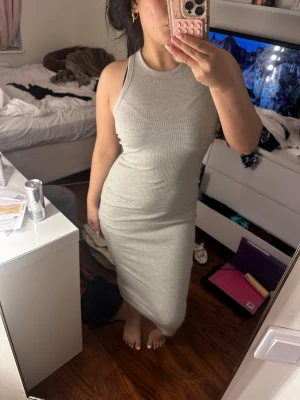 Grå ribbad ärmlös klänning - Snygg grå ribbad klänning med tight passform och ärmlös design. Klänningen har rund halsringning och är i ett stretchigt material som sitter skönt på kroppen. Perfekt för dig som gillar en enkel men stilren look.
