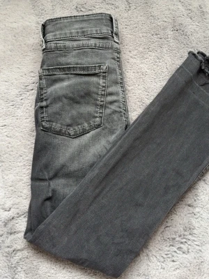 Gråa bootcut jeans med dubbla knappar - Snygga gråa lågmidjade jeans med dubbla knappar i midjan och klassiska fem fickor. Jeansen har slitningar och tvättade detaljer för en cool look. Tillverkade i stretchigt material för skön passform. Storlek 164. De har sytts upp en gång och sedan sprättas upp varav hur dom ser ut längst ner. Men skulle säga att de passar längden 150-155 cm💗