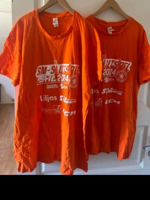 Orange SM-slutspel 2024 t-shirt - Säljer en orange t-shirt med trycket 'SM-slutspel SHL 2024' och flera loggor på framsidan. T-shirten har rund hals och korta ärmar, perfekt för dig som vill visa ditt stöd för laget.