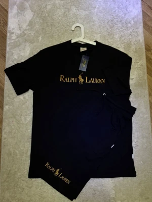 Svart set från Ralph Lauren - Svart sett från Ralph Lauren med logga och text broderat på bröstet. Helt ny med Prislappen kvar. Storlek XL men passae L. Perfekt för en clean och stilren look en fin sommarkväll. Tveka ej på att höra av dig!