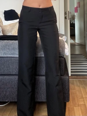 Svarta raka kostymbyxor - Snygga svarta kostymbyxor med rak passform och hög midja. Byxorna har bälteshällor, knapp och dragkedja framtill samt diskreta fickor. Perfekta för en clean och stilren look. En liten fläck framme men går säkert bort med lite vanish.