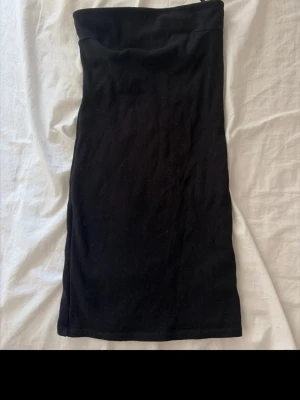 Svart axelbandslös kort klänning - Säljer en svart, axelbandslös kort klänning i enkel och stilren design. Klänningen har en tight passform och är perfekt för dig som gillar minimalistisk stil. Materialet känns mjukt och stretchigt, vilket gör den bekväm att bära.