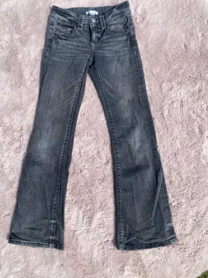 Grå bootcut jeans storlek 152  - Snygga grå jeans med bootcut passform och lätt slitna detaljer. Klassisk femficksmodell med dragkedja och knapp framtill. Perfekta för en avslappnad och trendig stil. från Gina Tricot