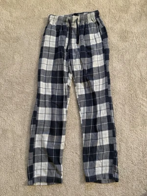 Rutiga pyjamasbyxor i blått och vitt - Pyjamasbyxor med rutigt mönster i mörkblått, grått och vitt. Byxorna har resår i midjan och raka ben. Tillverkade i mjukt tyg som känns skönt mot huden.