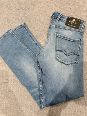 Replay anbass 32/32 - Snygga ljusblå jeans från Replay med raka ben och klassisk femficksmodell. Bakfickan har en unik mörkblå brodyr och en liten röd detalj. Jeansen har en tvättad look och är tillverkade i mjukt denimtyg. Storlek 32/32