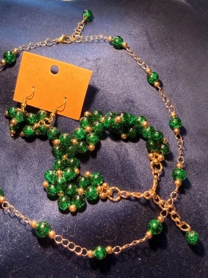 Set med halsband, örhängen och armband - Snyggt set med guldfärgad kedja och glittriga gröna pärlor. Kedjan har små guldfärgade kulor mellan de gröna pärlorna och justerbar längd. Perfekt för dig som vill ha en färgklick till din outfit.