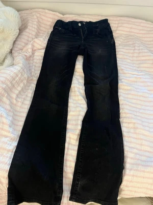 Lågmidjade svarta bootcut jeans - Säljer ett par svarta bootcut jeans med låg midja. Jeansen har en snygg tvättad look och är tillverkade i stretchigt denimtyg som sitter bekvämt. Perfekta för dig som gillar en tidlös och trendig stil.