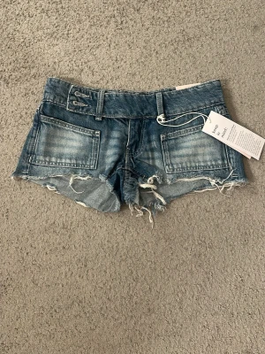 Blå denimshorts från Gina Tricot - Säljer dessa super snygga lågmidjade shortsen från Gina. Helt oanvända, lapparna sitter kvar. 