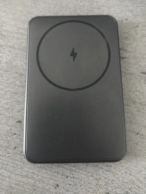 Svart MagSafe powerbank - En svart MagSafe-kompatibel powerbank med slimmad design och rund magnetisk yta för trådlös laddning. Utrustad med USB-C port och indikatorlampor på sidan. Perfekt för att ladda mobilen smidigt på språng. Med 5000mah