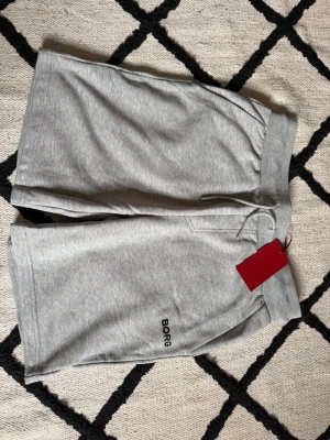 Grå sweatshorts från BORG - Snygga grå sweatshorts från BORG med elastisk midja och snörning. Shortsen har fickor på sidorna och en bakficka. Perfekta för en avslappnad stil och sköna att bära under varma dagar. Helt nya och oanvända! Original med kvitto 