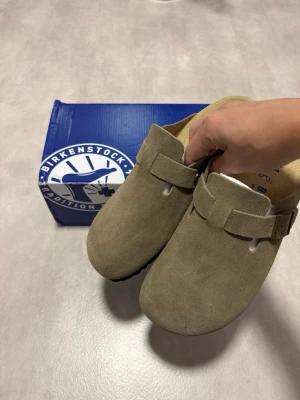 Birkenstock Boston Taupe Mocka Strl 41  - Säljer ett par Birkenstock Boston i taupe/mocka, storlek 41.  Använda endast ett fåtal gånger och i nytt skick. Sulorna har minimalt slitage och skorna är väl omhändertagna. Originalkartong medföljer, men den är något skadad.  Nypris ca 2 000 kr.  📦 Bud tas emot och fraktas inom 24h!