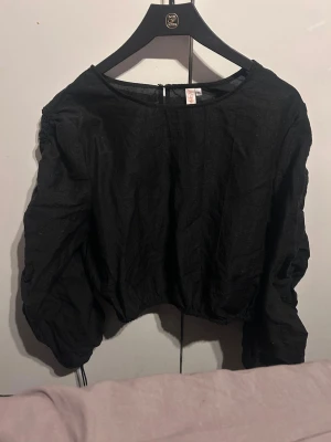Svart croppad topp från ONLY - Säljer en svart croppad topp från ONLY med långa puffärmar och rund halsringning. Toppen har en enkel och stilren design som passar perfekt till jeans eller kjol. Materialet känns lätt och luftigt.