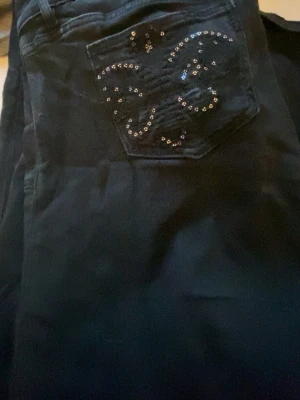 Svarta bootcut jeans med paljet detaljer. - Säljer ett par svarta low waist  bootcut jeans med detaljer på backfickan , framfickan. Har spruckit lite vid hällorna men kan sys enkelt.