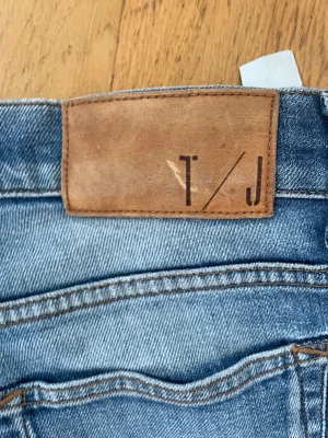 Blå slim  jeans från T/J - Säljer ett par blå skinny jeans från T/J med klassisk femficksdesign och snygga slitningar. Jeansen har en ljus tvätt och smal passform som sitter tajt längs benen. Perfekta för en trendig och avslappnad stil.