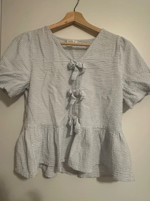 Randig peplum-topp från Gina Tricot - Säljer en blå/vit randig peplum-topp från Gina Tricot i storlek S. Toppen har korta puffärmar och tre fina rosetter framtill. Materialet är mjukt och skönt. Jättefint skick.