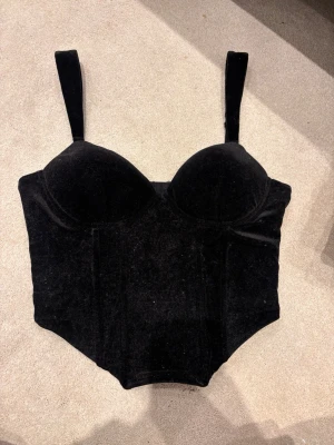 Svart sammetskorsett / corset top  - Svart sammetskorsett / corset top 🖤 Säljer en svart korsettliknande topp i sammetsmaterial. Köpt second hand, så jag vet tyvärr inte vilket märke det är eftersom lappen är bortklippt. Storlek 36, passar ungefär S/M.  Använd men i fint skick. Materialet drar väldigt lätt åt sig damm och ludd, vilket är vanligt för sammet. Det försvinner inte i tvättmaskinen, utan behöver tas bort för hand, t.ex. med en klädroller eller luddborste. Som syns på bilderna. skriv vid intresse eller frågor! 