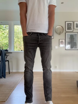 Jack & Jones glenn Svart/gråa - Säljer ett par svarta slim fit jeans med klassisk femficksmodell och snygg tvätt. Jeansen har smal passform och raka ben, perfekta till en avslappnad stil. Materialet är mjukt och stretchigt för extra komfort.