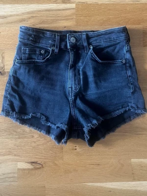 Svarta jeansshorts från H&M  - Säljer ett par svarta jeansshorts från H&M Divided i storlek 34. Shortsen har hög midja, råa kanter och klassisk femficksdesign. 