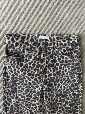 Leopardmönstrade jeans från Sinsay - Leopardmönstrade jeans från Sinsay i storlek 36. Jeansen har klassisk femficksmodell, knappgylf och bälteshällor. Materialet är denim med stretch för extra komfort. Perfekta för dig som vill sticka ut med ett djuriskt mönster.