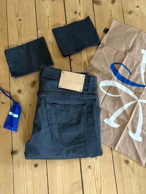 Mörkgrå jeans från Jacob Cohen - Snygga mörkgrå jeans från Jacob Cohen med klassisk femficksmodell och raka ben. Jeansen har diskreta sömmar och patch med logga bak i midjan. Tillverkade i mjukt denimtyg som ger en skön känsla och stilren look.