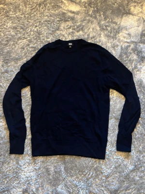 Mörkblå stickad tröja - En enkel och stilren mörkblå stickad tröja med rund hals och långa ärmar. Tröjan har ribbade muddar vid ärmslut och nederkant. Perfekt att matcha med jeans eller kjol för en clean look.