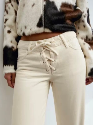 Vida beige jeans med snörning fram - Säljer ett par trendiga beige jeans med hög midja och unik snörning framtill. Byxorna har raka, vida ben och klassiska fickor. Perfekta för dig som vill sticka ut med en cool detalj och samtidigt ha en avslappnad look.