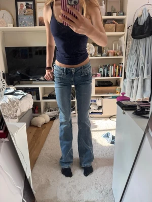 Ljusblå bootcut jeans med låg midja - Säljer ett par ljusblå jeans med bootcut och låg midja. Jeansen har klassiska fem fickor, slitningar och en snygg tvättad look. Perfekta för dig som gillar en avslappnad och trendig stil. Storlek 170! 