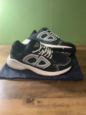 Svarta Dior sneakers med vit sula - Snygga svarta sneakers från Dior med vit och grå detaljering samt tjock vit sula. Skorna har en sportig design med mesh och läderpaneler, samt tydlig Dior-logga på sidan och sulan. Perfekta för dig som gillar streetwear och exklusiva märken.