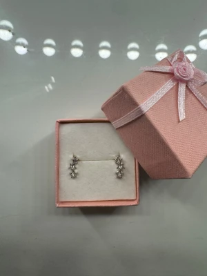 Stjärnformade örhängen med stenar - Säljer ett par snygga örhängen i silverfärg med tre små stjärnor på varje örhänge. Varje stjärna har en glittrande sten i mitten som ger extra bling. Perfekta för dig som gillar unika detaljer och vill sticka ut lite extra.