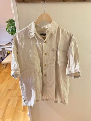 Beige bommulsskjorta  med kort ärm Tommy hilfigher  - Snygg beige skjorta i bommul med korta ärmar och klassisk krage. Skjortan har bröstficka och knappar framtill. Perfekt för en avslappnad och stilren look.