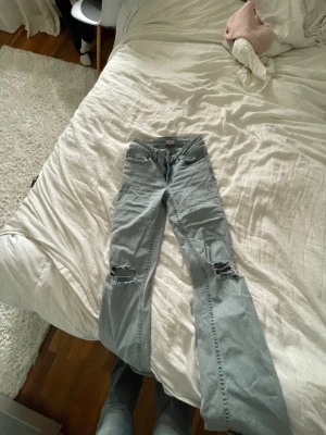 Nelly jeans - Säljer ett par ljusblå jeans med raka ben och stora hål vid knäna. Jeansen har klassisk femficksmodell och är tillverkade i denim. Perfekta för en avslappnad och trendig look.
